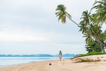 girl walks along the beach, tropical samui island in thailand, exotic place for tourism and travel, blue sea and yellow sand, coconut trees on the seashore