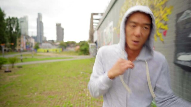 Chinese runner and boxer jogging and air boxing, workout in a city park in a fitness training session with graffiti street art wall and London city skyscrappers in the background