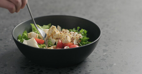 man hand pick salad with mozzarella, cherry tomatoes and frisee leaves in black bowl on terrazzo surface