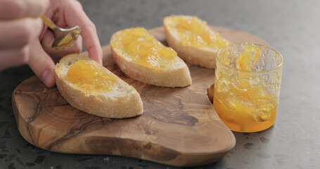 man spreading orange marmalade on ciabatta slices on wood board