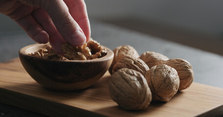 man hand take walnut kernels from wooden bowl
