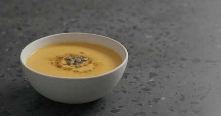pumpkin cream soup in white bowl on terrazzo countertop