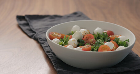 salad with kale , cherry tomatoes and mozzarella in white bowl