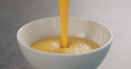 Pour pumpkin cream soup in a white bowl on concrete backdrop