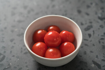 ripe cherry tomatoes in white bowl on concrete surface