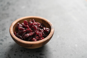 Dried cranberries in olive wood bowl on concrete surface