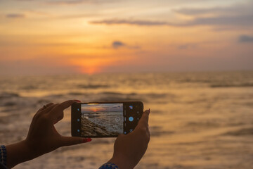 A tourist trying to take the picture of beautiful sunset through the horizon from the seashore in Bali