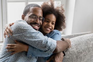 Obraz premium Affectionate loving young african american father cuddling little smiling biracial child daughter, enjoying sweet tender moment together indoors, copy space, happy family showing care and devotion.