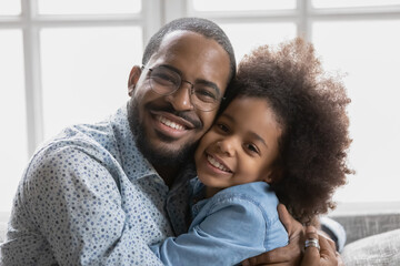 Head shot close up portrait of happy loving african ethnicity father embracing smiling cute school...