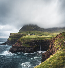 Gasadalur village and Mulafossur its iconic waterfall, Vagar, Faroe Islands, Denmark. Rough see in the north atlantic ocean. Lush greens during summer.