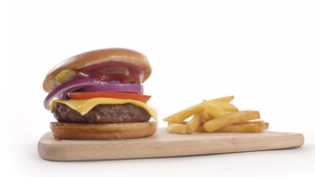 Tasty burger with french fries fall and assembled from ingredients on white background. Isolated. Burger is made from juicy beef meat, lettuce, leaf, onion, tomato, american cheese, pickles separately