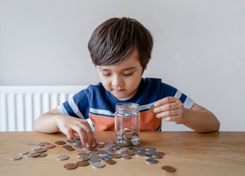 School Kid putting money coins into clear jar, Child counting his saving money, Young boy holding coin on his hands, Children learning about saving for future concept