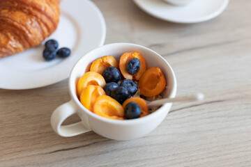 Delicious milk oatmeal with apricots and blueberries in a white bowl on a wooden table in the kitchen