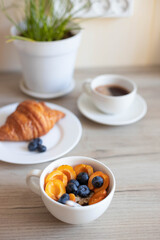 Delicious milk oatmeal with apricots and blueberries in a white bowl on a wooden table in the kitchen. Vertical photo