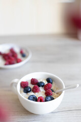 Delicious milk oatmeal or muesli with raspberries and blueberries in a white bowl on a wooden table in the kitchen