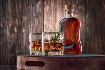 Two square glasses of whiskey with ice and a sprig of rosemary, and a full bottle of whiskey, stand...
