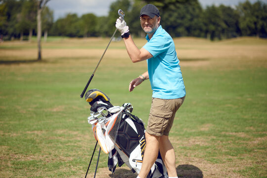 Middle-aged man playing a round of golf on a golf course turning to smile at the camera as he selects a club from his bag for the next shot