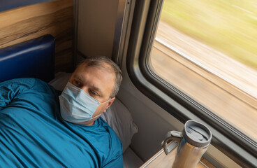 man in a medical mask near the train car. concept of travel during the pandemic. passenger is lying in his seat in the compartment of the car