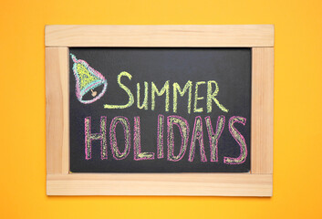 Chalkboard with phrase SUMMER HOLIDAYS on orange background, top view. School's out