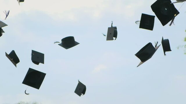 Close up in slow motion of university high school graduates throwing their square academic Tudor bonnet cap into the air graduation ceremony. Students Celebration of a MBA bachelor and master degree