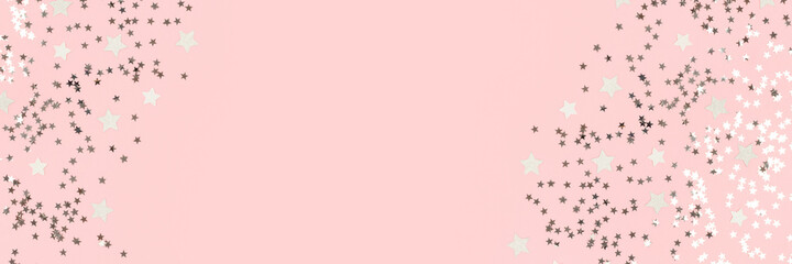 Border frame made of silver stars confetti on a pink pastel background. Banner with place for text.