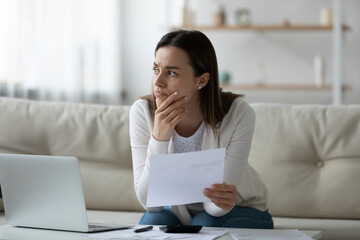 Stressed millennial woman holding banking paper letter, thinking of financial problems alone at home. Thoughtful unhappy young lady having difficulties with managing budget, bankruptcy concept.