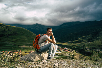 Naklejka premium Tired traveling man resting on hill. Exhausted male tourist sitting on stone after active trekking in mountains