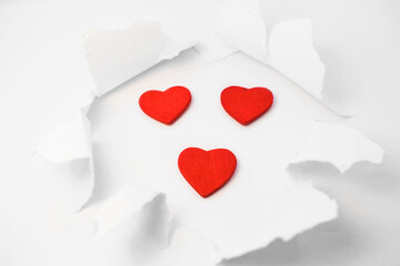 on a white background - a white sheet of paper, torn in the center in the form of a ragged circle. In the center of the circle are three small red hearts. Banner, greeting card love
