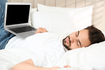 Lazy young man with laptop sleeping on bed at home