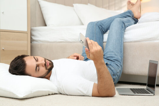 Lazy young man with laptop and smartphone lying on floor at home