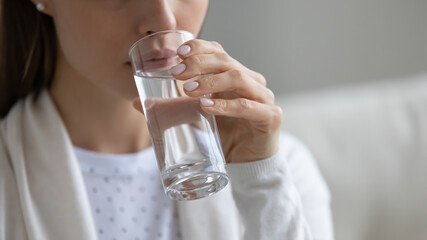 Close up young healthy woman drinking glass of pure clear stilled water. Millennial lady enjoying daily habit, hydrating organism with aqua, maintaining bowel function, skincare healthcare lifestyle
