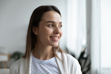 Head shot close up dreamy young smiling beautiful woman looking away, visualizing future indoors of...