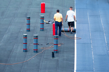 Roof waterproofing. Two workers are working on installation of waterproofing layer. Man next to rolls of bitumen insulating layer. Roof cover replacement. installation bitumen insulating layer.