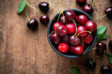 Fresh ripe sweet cherries in a bowl with droplets of water. Overhead view on dark rustic wooden background, closeup