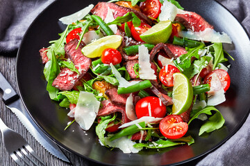 Beef tagliata salad on a black plate, close-up