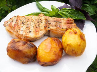 roast pork steak on a plate with potatoes and herbs. rosemary.
