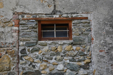 Fototapeta na wymiar Alte Steinwand aus rohen Steinen mit Holzfenster, Stallwand aus Kalkstein mit Stallfenster