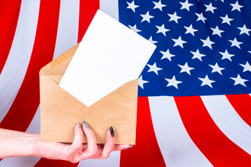 Fototapeta na wymiar Election of the President of the United States. A woman hand with a ballot for the American Presidential election. Envelope with a Bulletin on the background of the us flag. US Elections 2020.