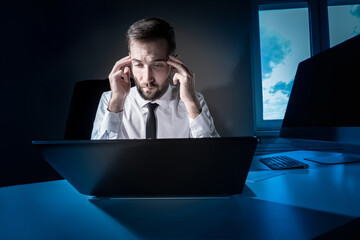 Tired worker. A tired businessman works in the evening. A man in office clothes is holding his temples. Problems in business. The businessman is trying to solve the problems that have arisen.