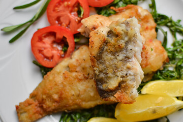 Fried fish fillet with tomatoes, lemon and rosemary. White plate. Light background. Close-up.