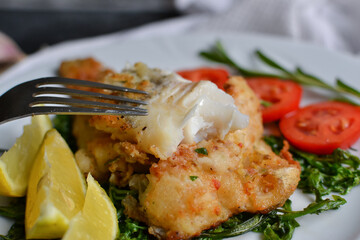 Fried fish fillet with tomatoes, lemon and rosemary. White plate. Dark background. White linen napkin.