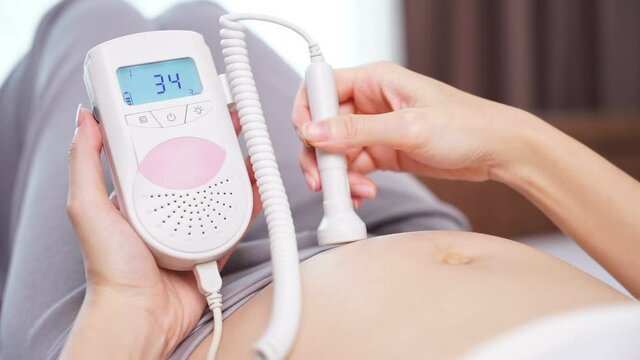 asian woman using pocket fetal doppler to monitor baby heart beat. expectant mother scan and examine belly.