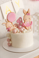 Birthday decorations - gifts, toys, balloons, garland and figure for little baby party on a white wall background. Cake with rabbit figure.