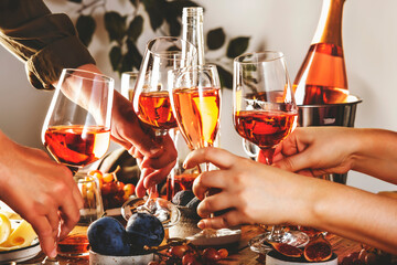 Hands holding glasses with rose wine over the table served for festive dinner party with different kinds of appetizers and fruits