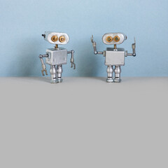 Robots communication. Two simplified metal silver robotics toys on light blue wall, gray floor background. Copy space.