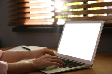 Woman using modern laptop at wooden table indoors, closeup