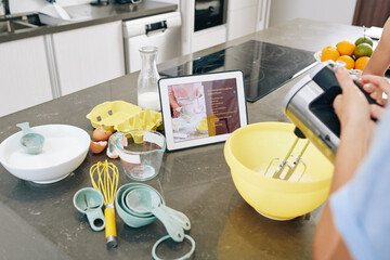 Housewife following recipe on tablet computer and mixing ingredients in plastic bowl