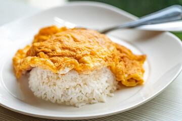 Easy Thai food menu, Thai omelette over rice or Kai Jeaw Rad Kow. Close up Thai omelette over white rice in white plate on table.