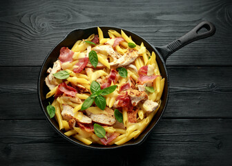 Chicken, bacon Penne pasta with cheese and basil in iron cast. healthy food.