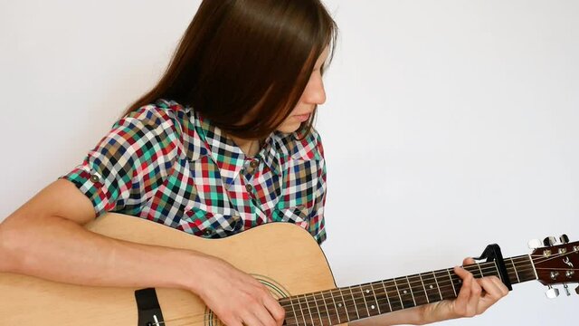A beautiful young lady dressed in a color checkered shirt plays an acoustic guitar against white background